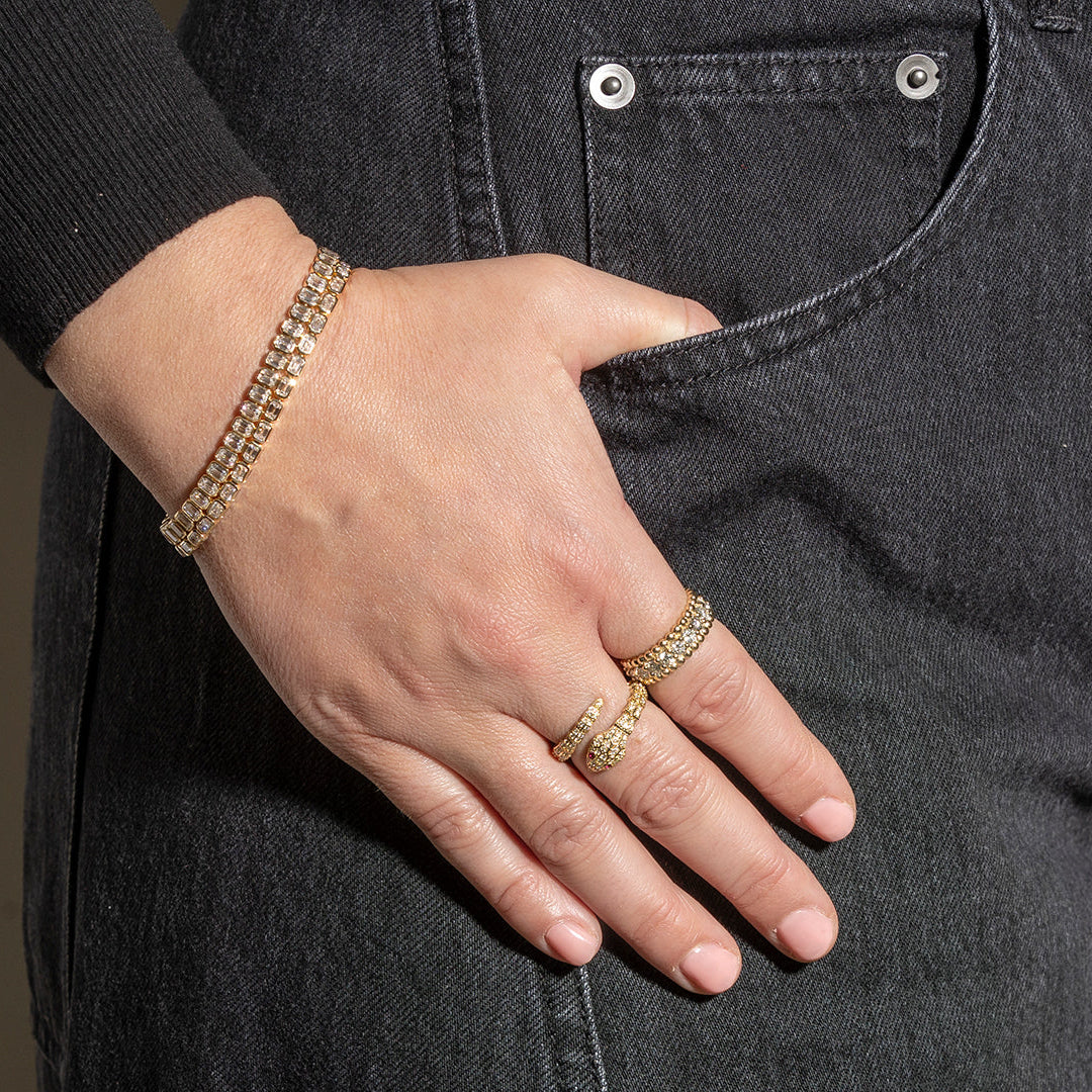Hand wearing gold bracelets and rings on a dark denim background
