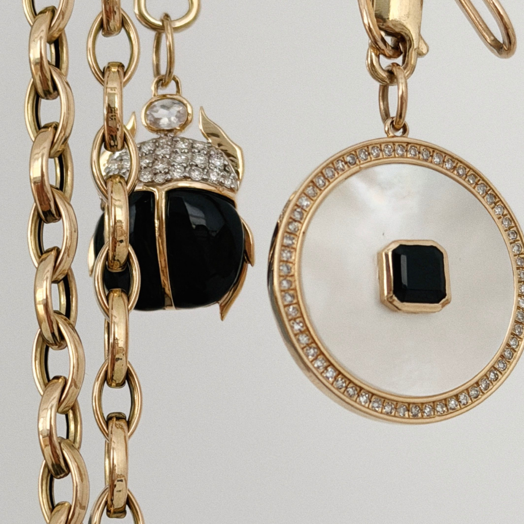 14k gold chains and two onyx and mother of pearl pendants with a white background.