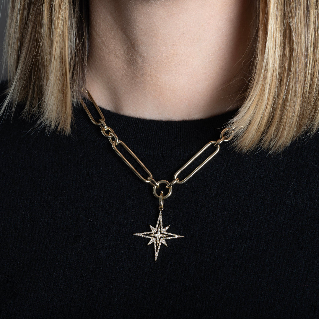 A person wearing a chunky link chain with a diamond pave starburst pendant.