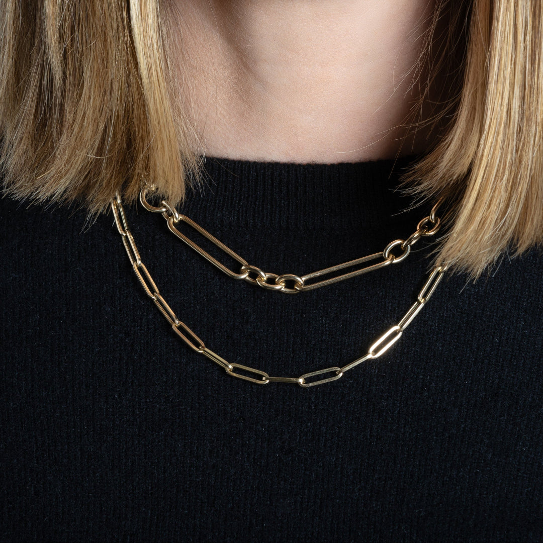 A person wearing two 14k gold chains, one chunky mixed length and one paperclip style.