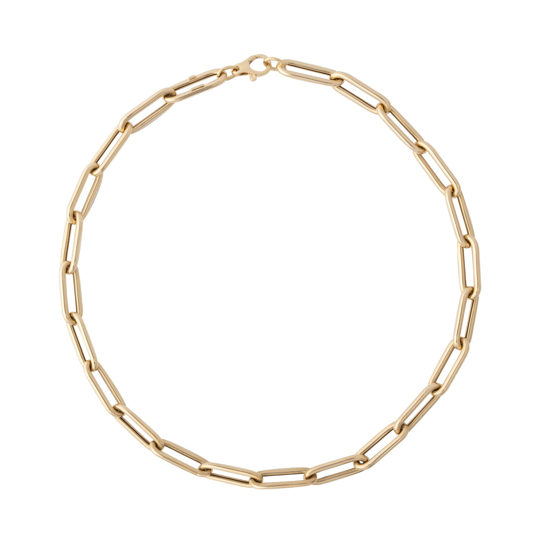 A chunky gold paperclip chain necklace laid out on a plain background.