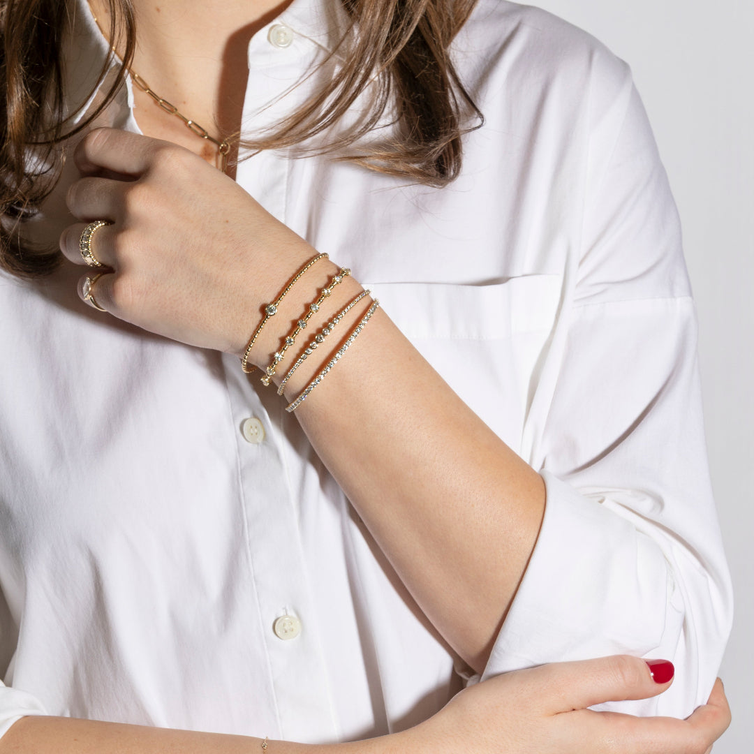Close-up of a person wearing multiple gold bracelets on a white shirt background