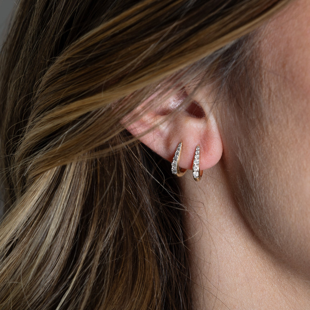 Two 14k gold Claw Diamond Huggie Earrings with a V-shaped design and diamond embellishments on someone's ear.