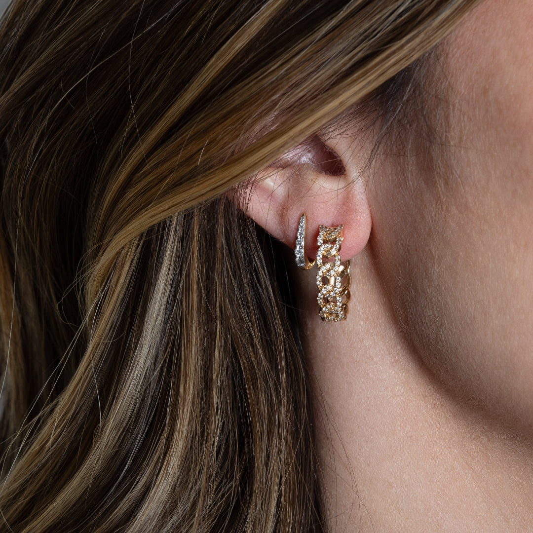Two 14k gold earrings, one Claw Diamond Huggie Earring with a V-shaped design and diamond embellishments and one curb chain diamond pave Hoop Earring on someone's ear.