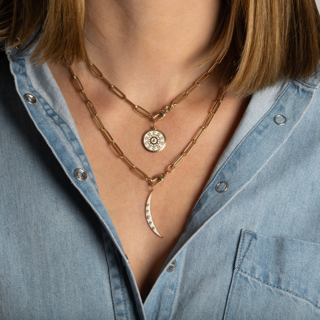 A person wearing two gold paperclip chain necklaces, each with white enamel pendants.
