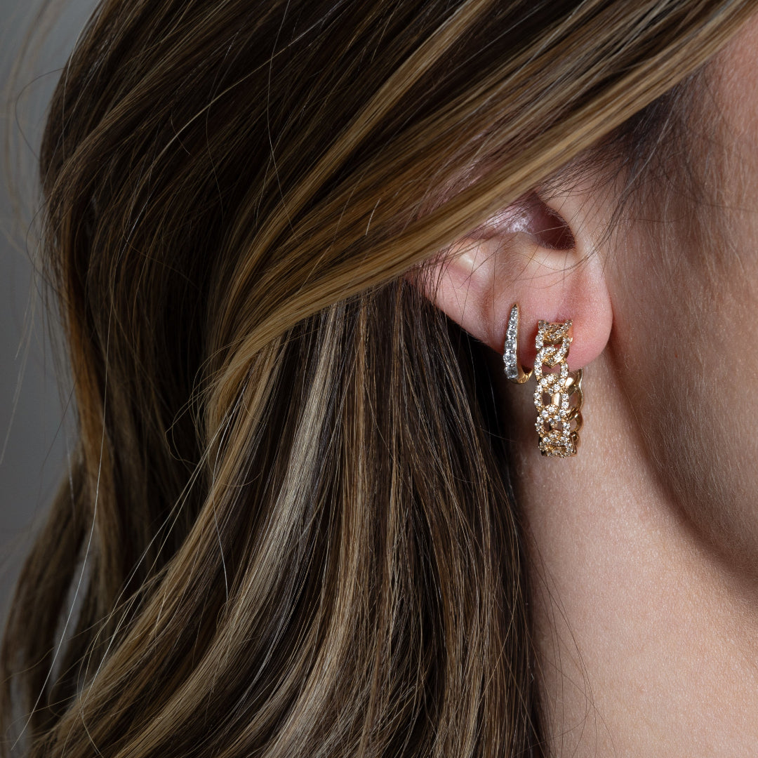 A person wearing curb chain style diamond earrings layered with smaller huggie earrings.