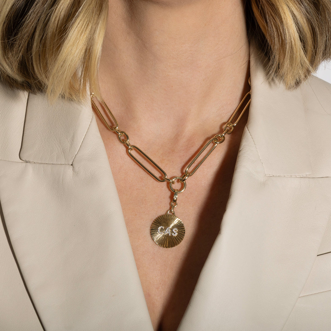 Gold necklace with pendant on a person wearing a beige blazer.