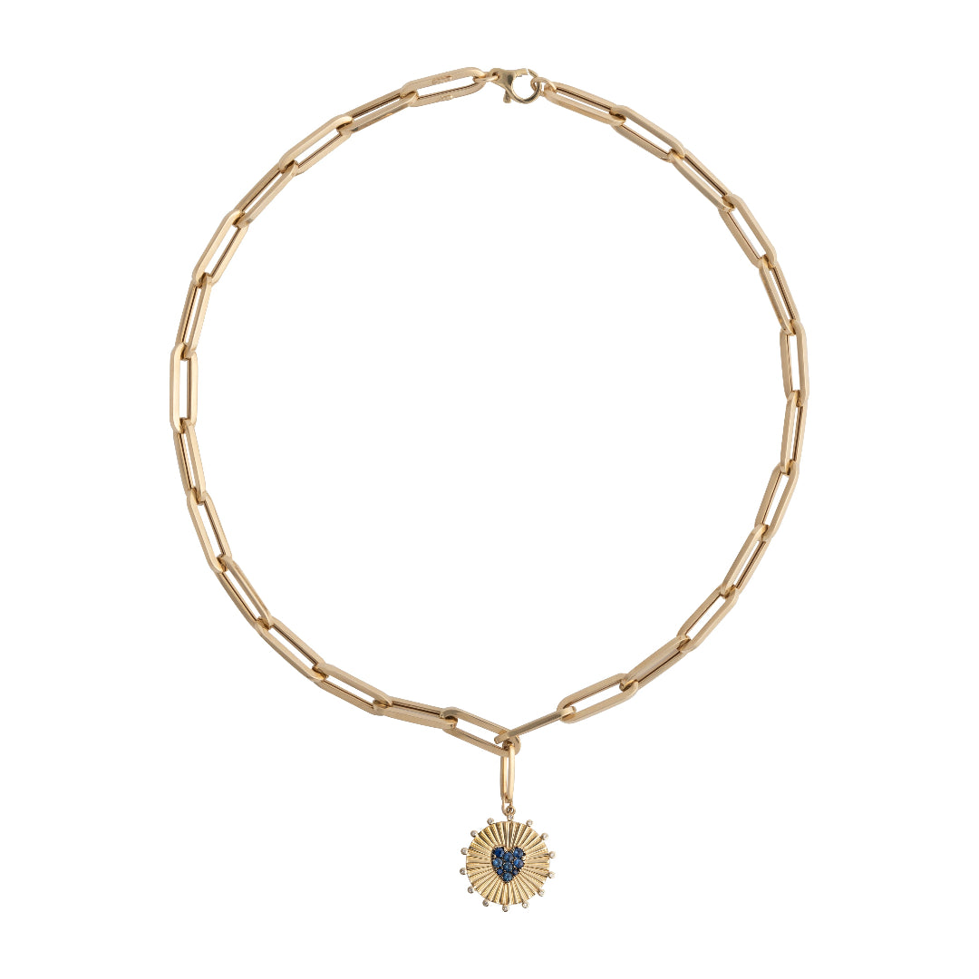 A paperclip chain necklace with a gold pendant with a blue sapphire heart attached with a pendant bail, laid out on white background.