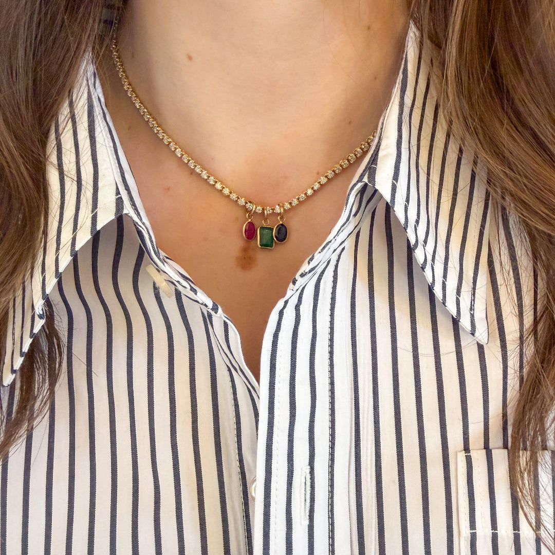 A person wearing a striped shirt and tennis necklace with pendants made of emerald, ruby and blue sapphire.