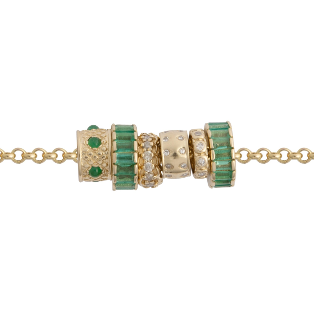 A gold chain with emerald and diamond beads on a white background.