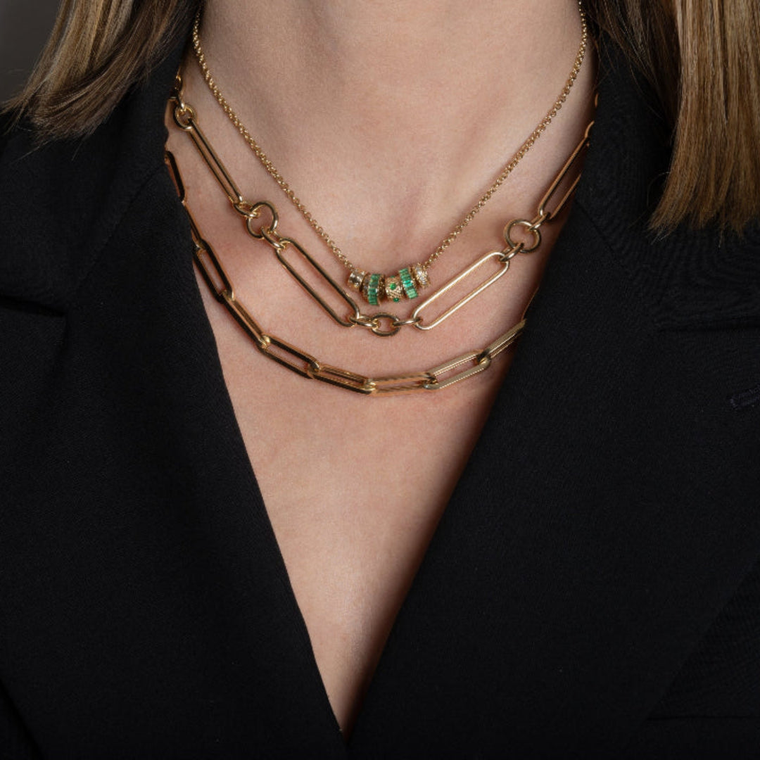 Close-up of a person wearing gold necklaces with emerald beads against a black background.