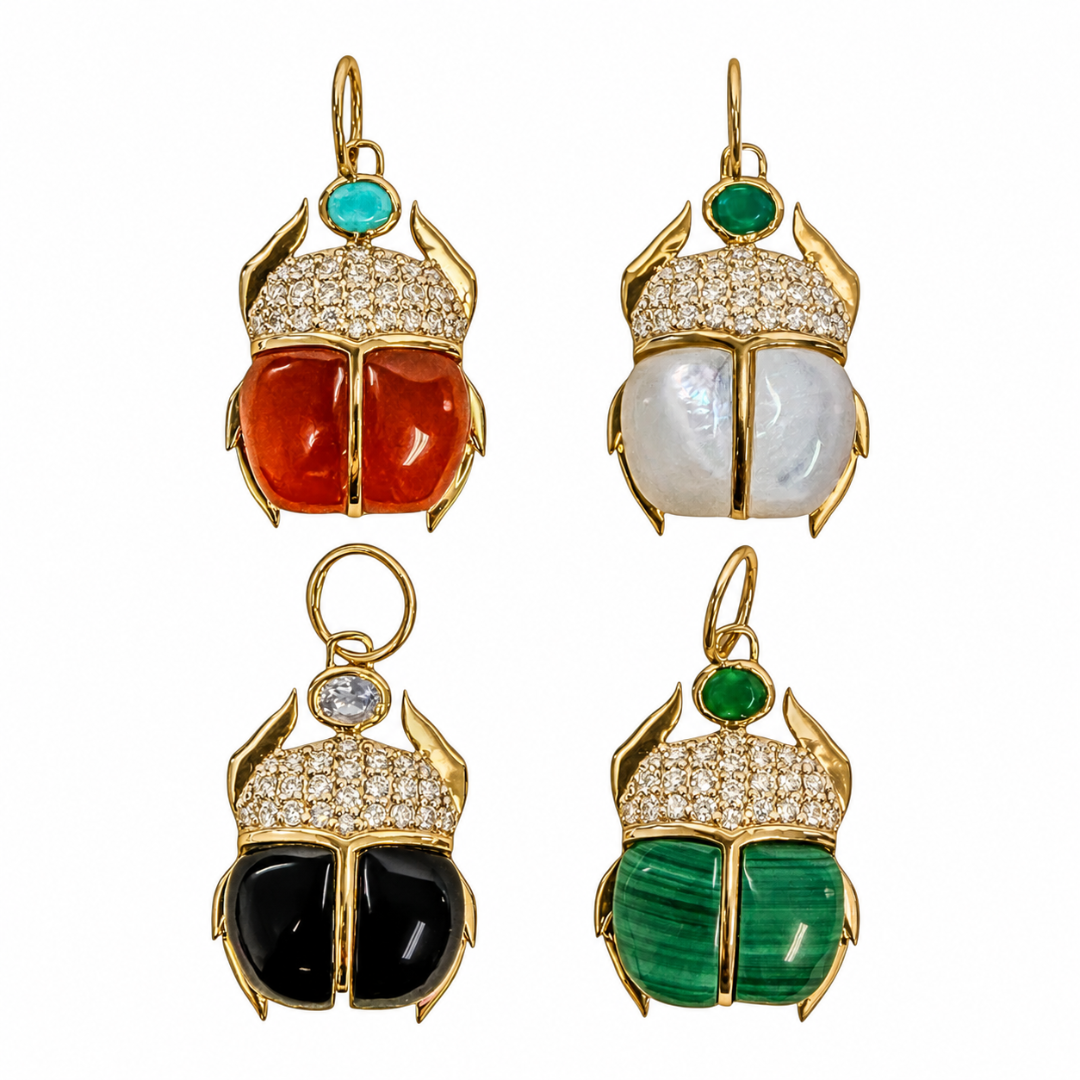 Four 14k gold scarab-shaped pendants arranged on a white background. Each scarab features a 14k gold setting with pavé-set diamonds stones, a small colored stone at the top, and a two-tone beetle body: two pairs are red and black, and two pairs are white and green.