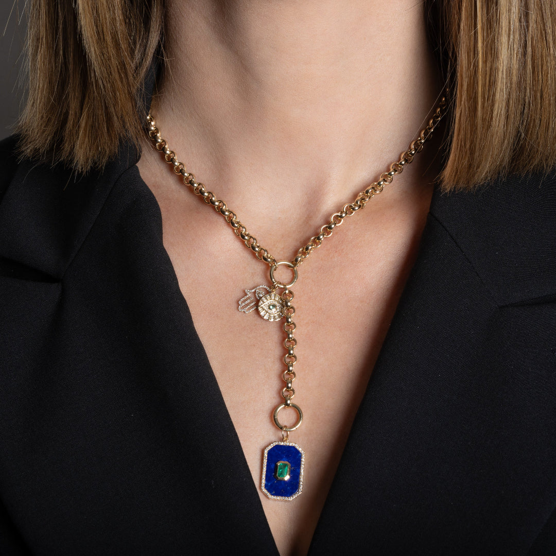 A person wearing 14k gold rolo lariat necklace with a 14k gold Hamsa diamond mini pendant and a larger lapis, emerald and diamond rectangle pendant