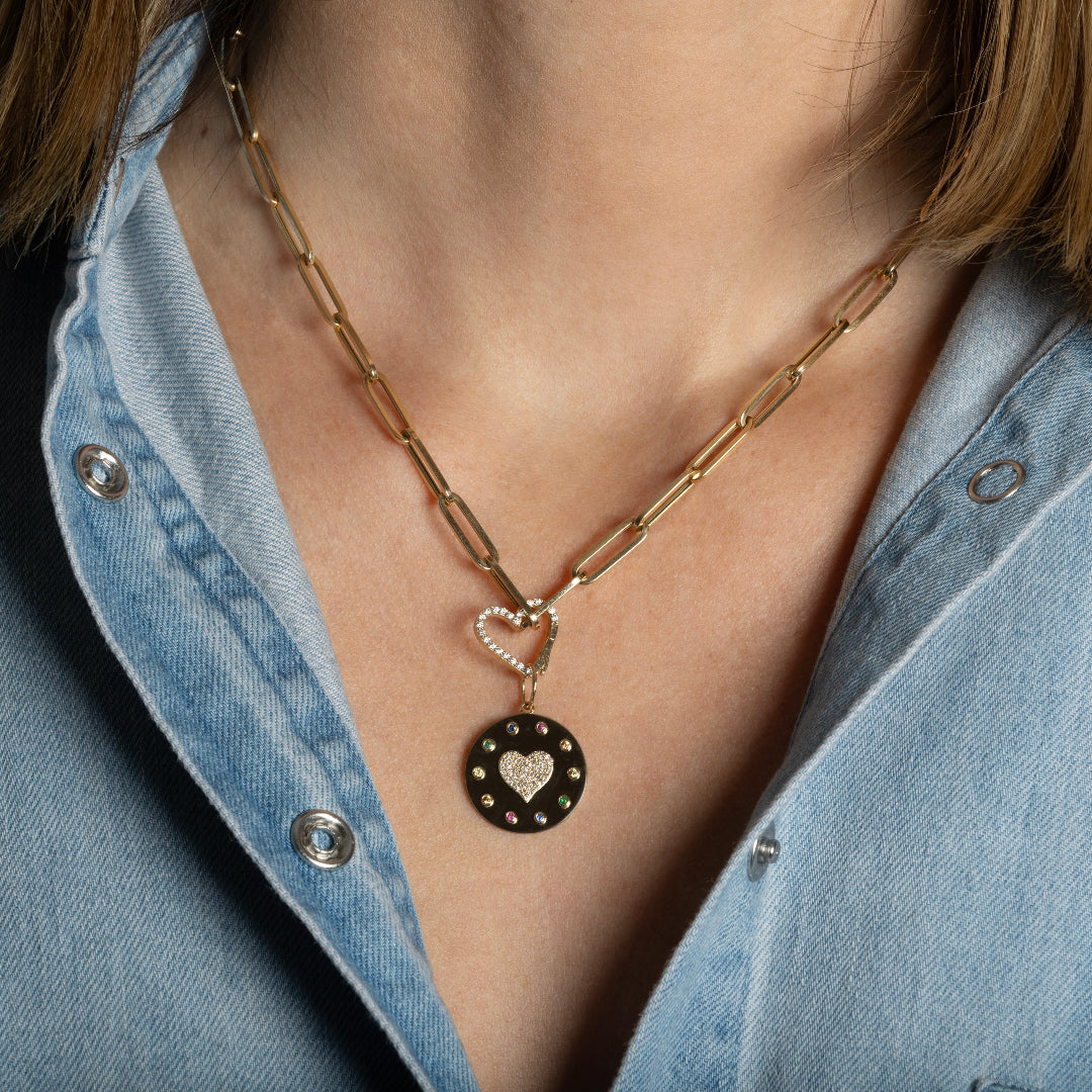 A person wearing a paperclip chain necklace with a heart shaped gold and diamond pendant attached by a heart shaped diamond pave pendant bail.