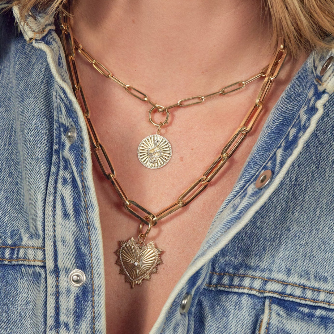 A person wearing a 14k gold paperclip chain necklace with a 14k gold diamond serpent charm layered with a 14k gold chunky paperclip necklace and a 14k gold beveled heart charm.
