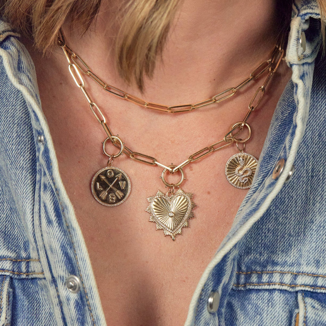 A person wearing two layered 14k paperclip chain necklaces, one adorned with charms.