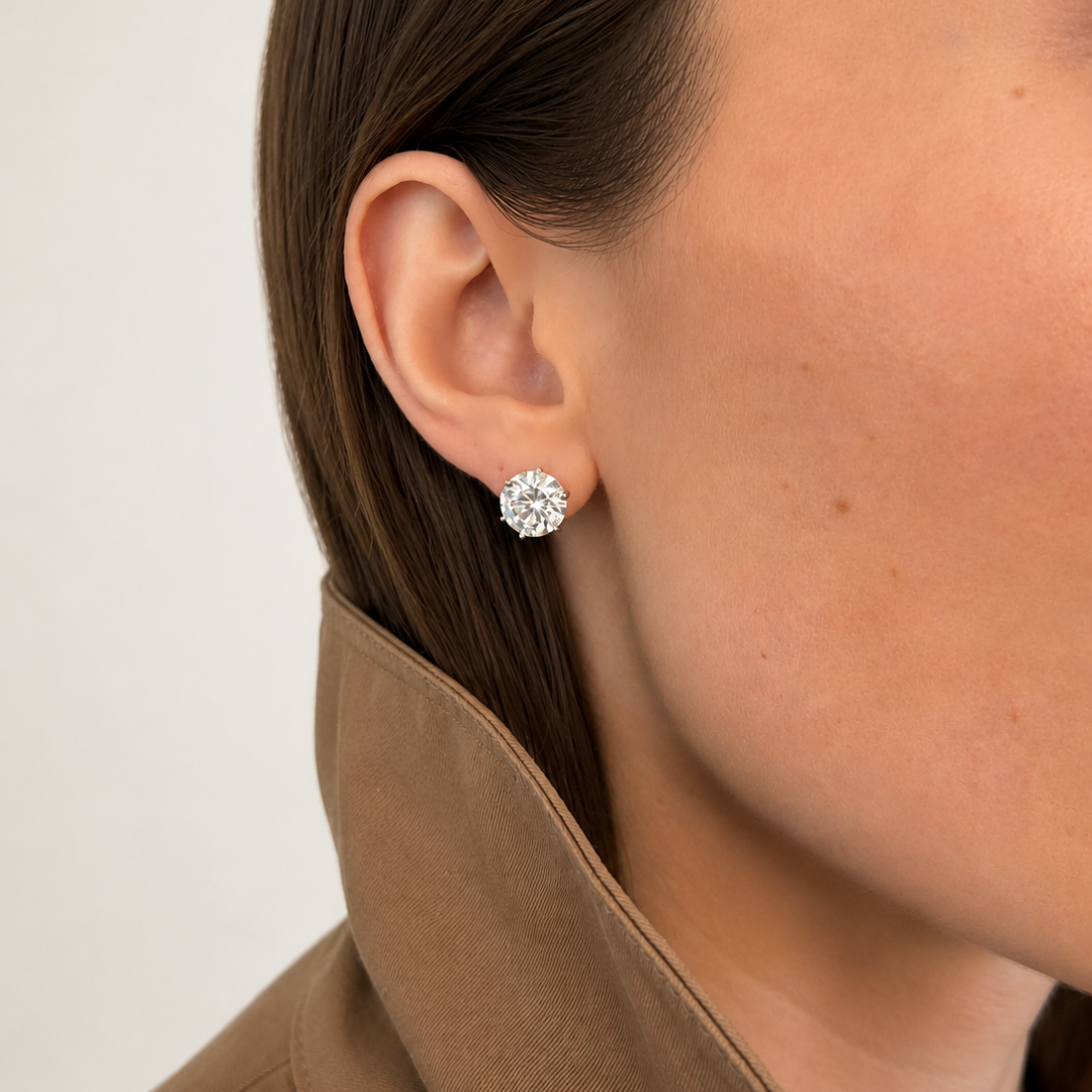A close-up of a model's ear wearing a lab-grown stud in a 14k white gold martini setting, paired with a brown coat against a light neutral background.
