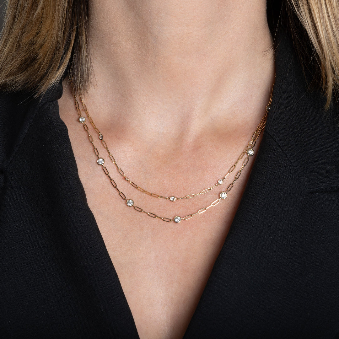 A person wearing two 14k gold diamond station paperclip chain necklaces layered together.