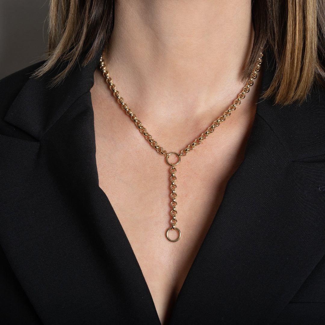 A person wearing a gold lariat style necklace made with a rolo chain.