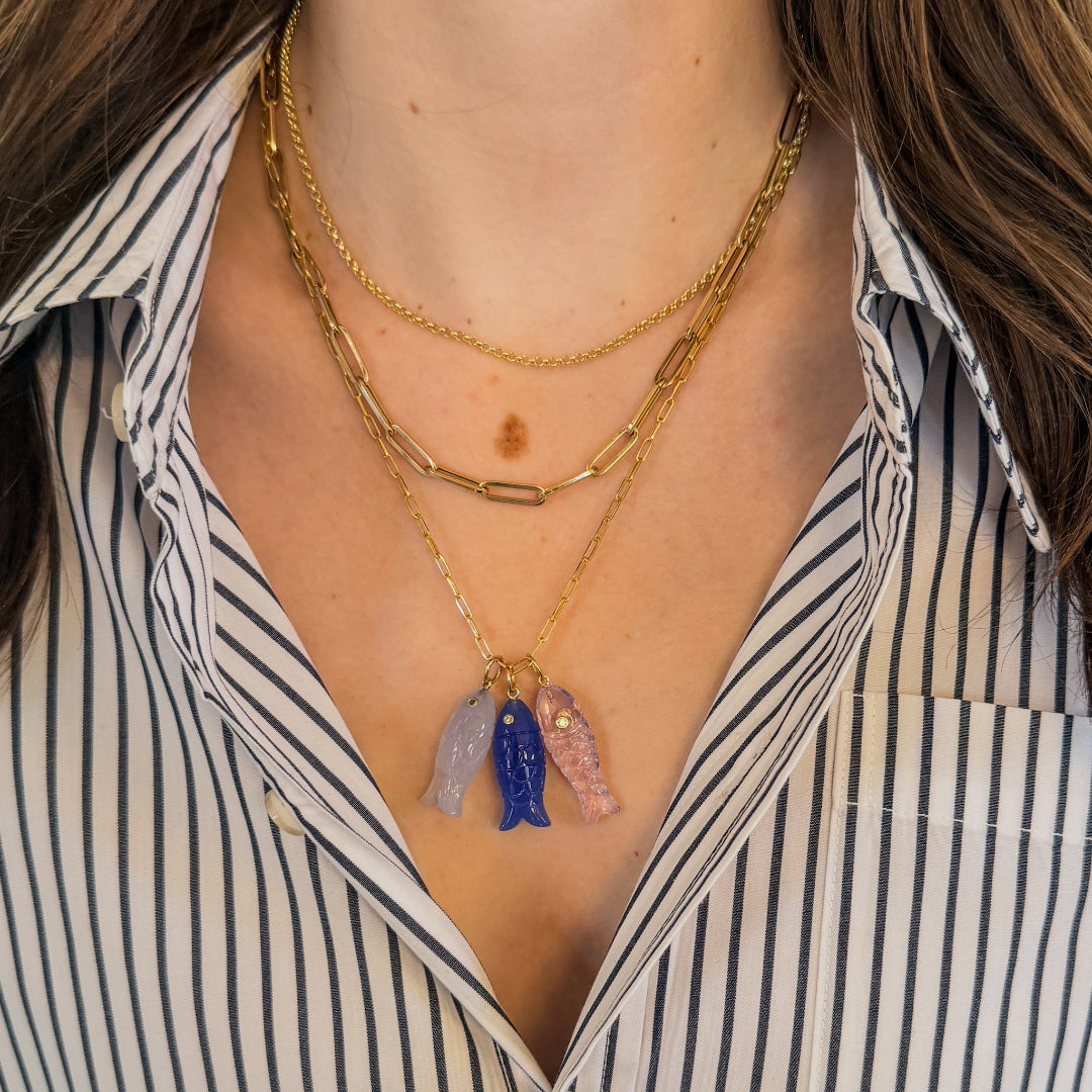 Person wearing a striped shirt and three 14k gold necklaces. One of the gold chains has three colorful fish pendants on it.