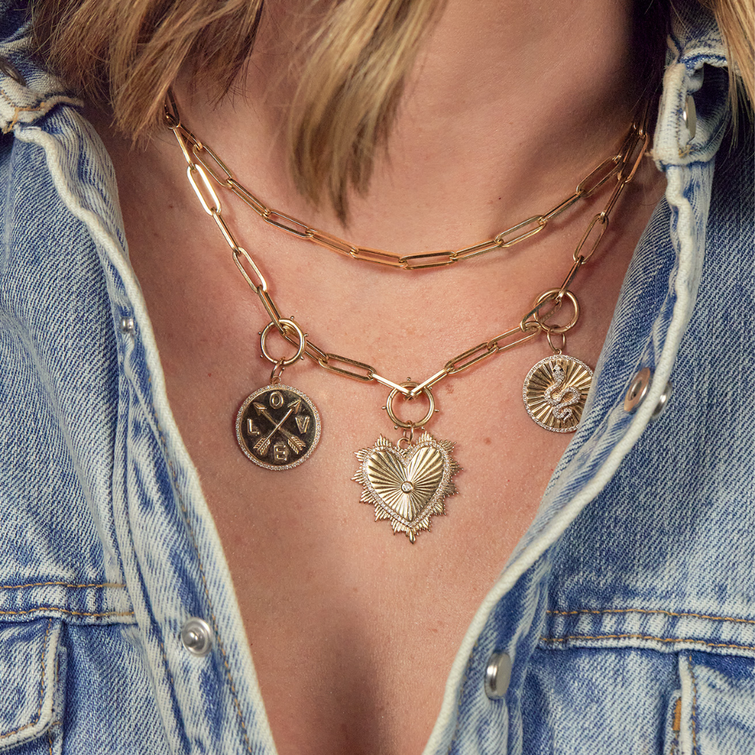 A person wearing two gold paperclip chains, one with three different gold pendants.