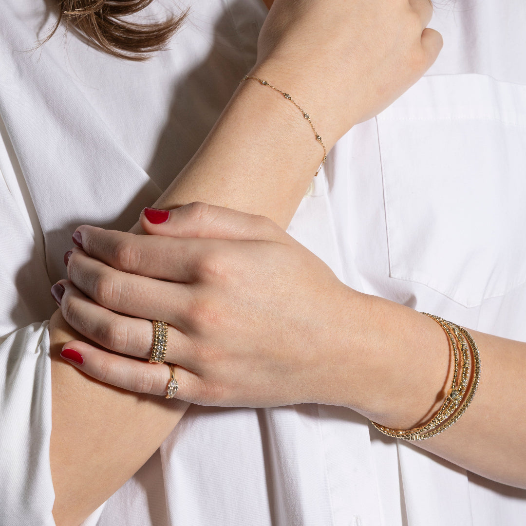 Close-up of a person's wrist and hand wearing gold jewelry on a white background