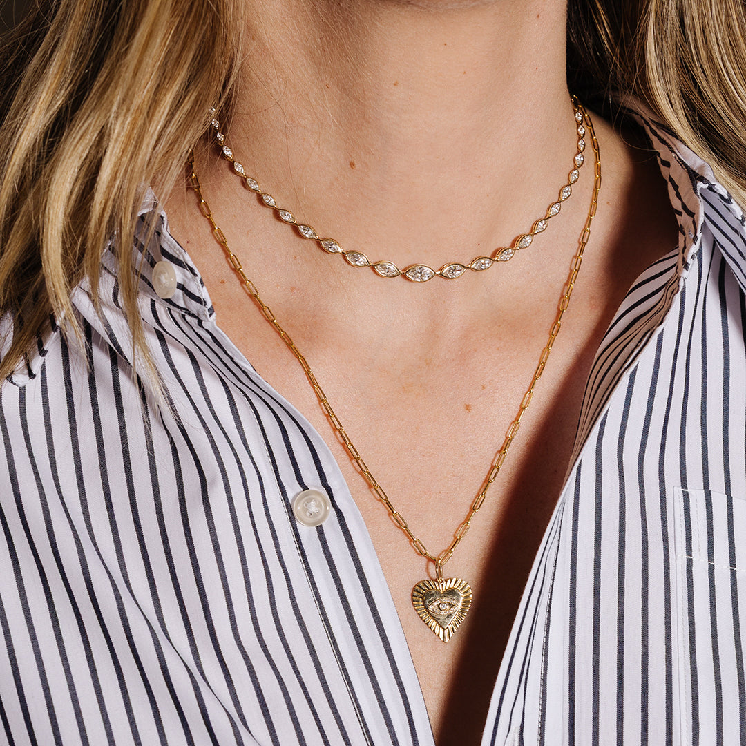 Close-up of a person wearing gold jewelry including a necklace, bracelet, and ring, with a striped shirt.