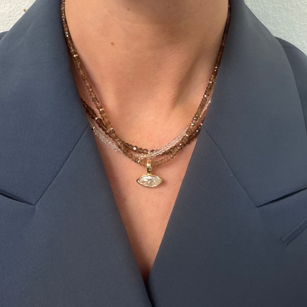 A person wearing a blue blazer and three gemstone necklaces with a bezel-set marquise pendant.