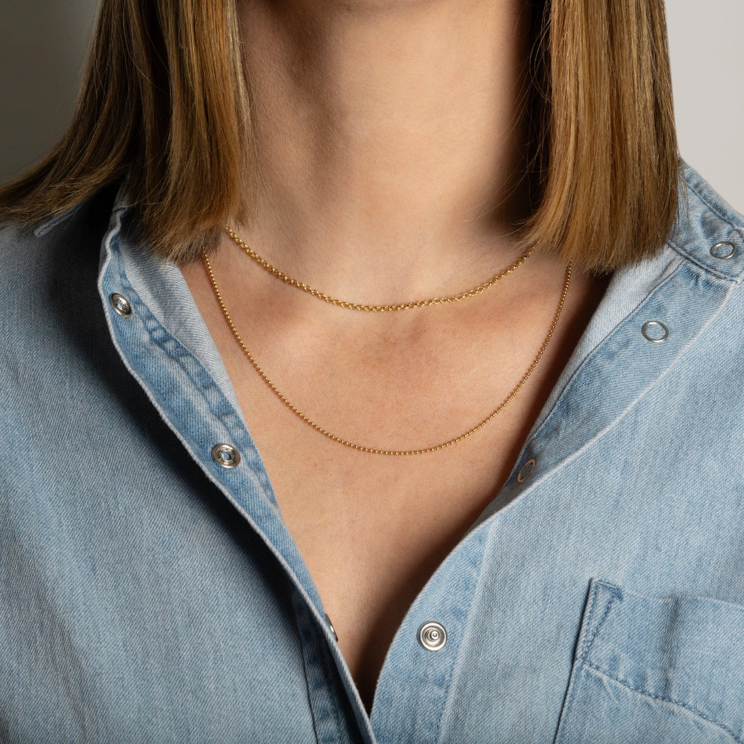 A person wearing a denim shirt layered with two 14k gold gold chains.