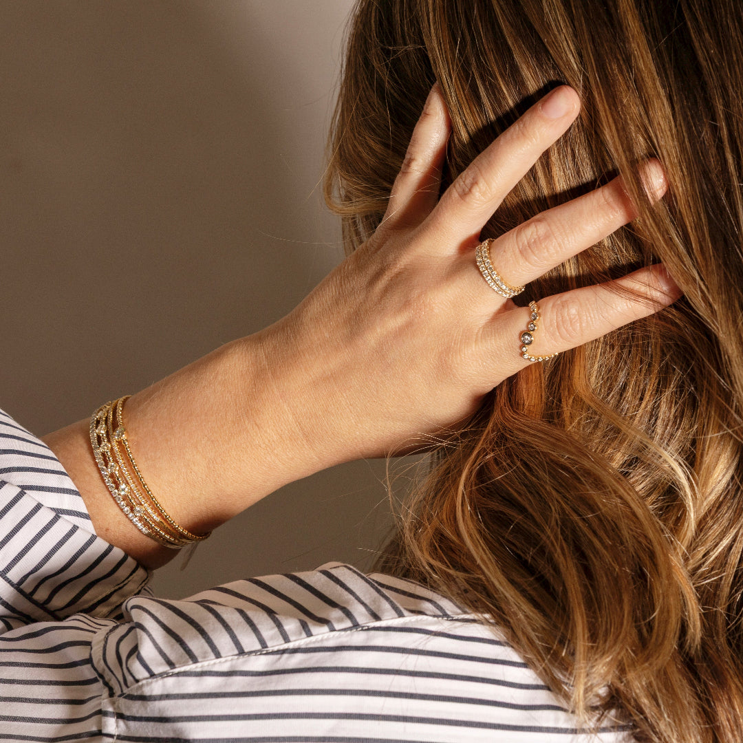 Hand with gold jewelry touching hair against a neutral background