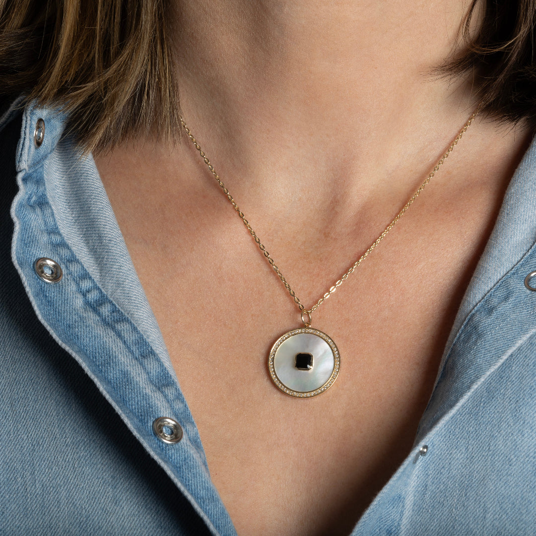 A person wearing a thin gold chain with a Mother of Pearl, Diamond and Black Onyx Pendant.