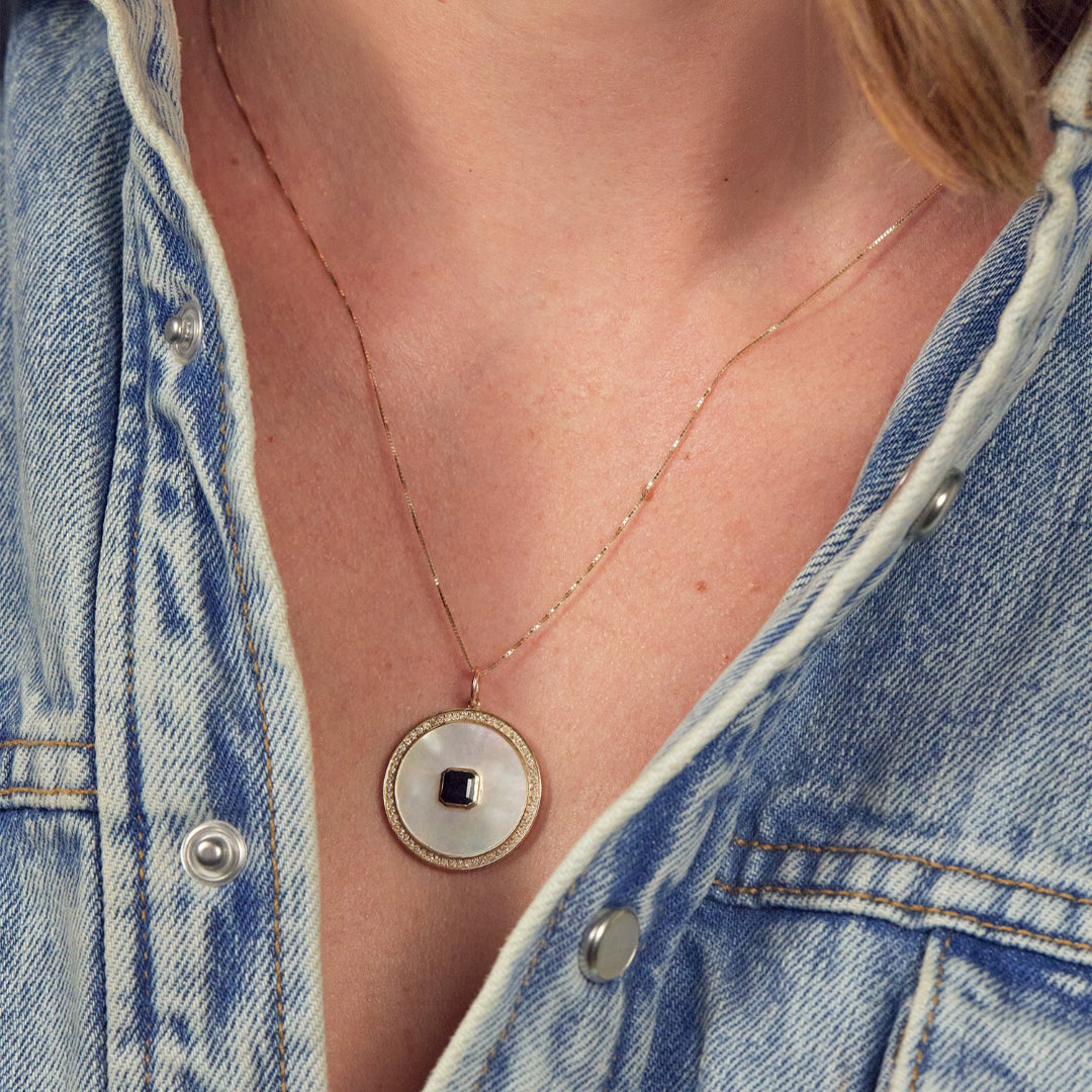 A person wearing a thin gold chain with a Mother of Pearl, Diamond and Black Onyx Pendant and a denim shirt.