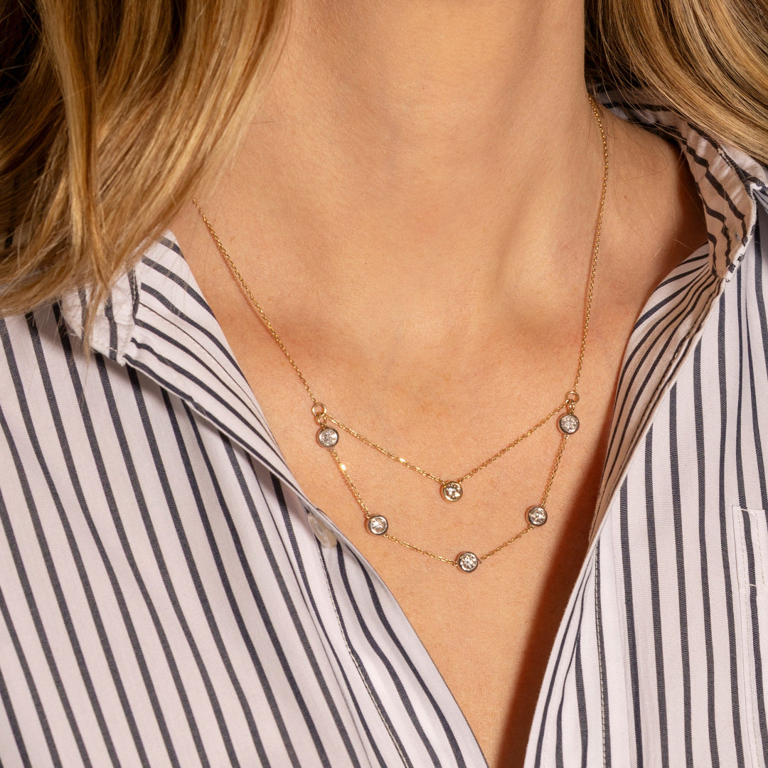 Gold necklace with white and yellow gold bezels worn by a person in a striped shirt