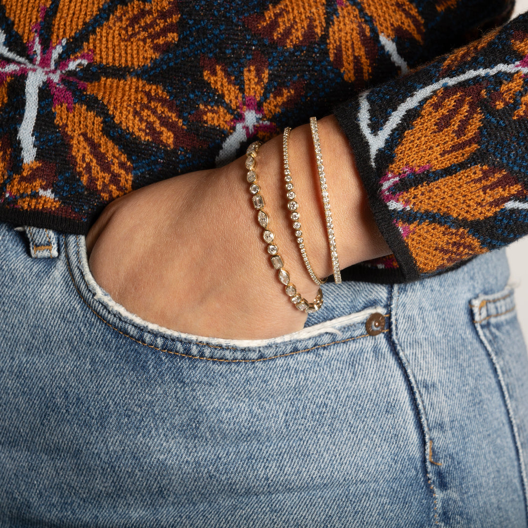 A person wearing three diamond tennis bracelets with their hand in their jean pocket.