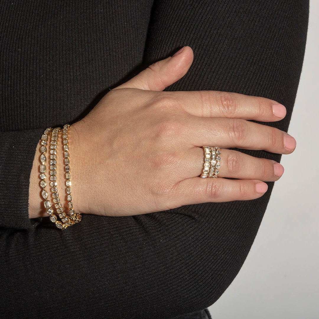 A person wearing three diamond tennis bracelets and three stackable rings.