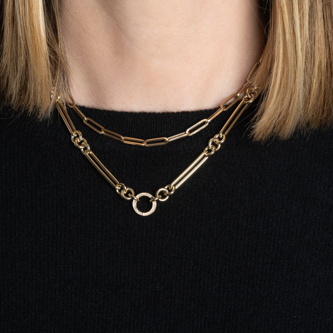 A person in a black sweater wearing a 14k gold necklace with a double-sided diamond enhancer, featuring oval and round link chains layered with a gold paperclip chain necklace.