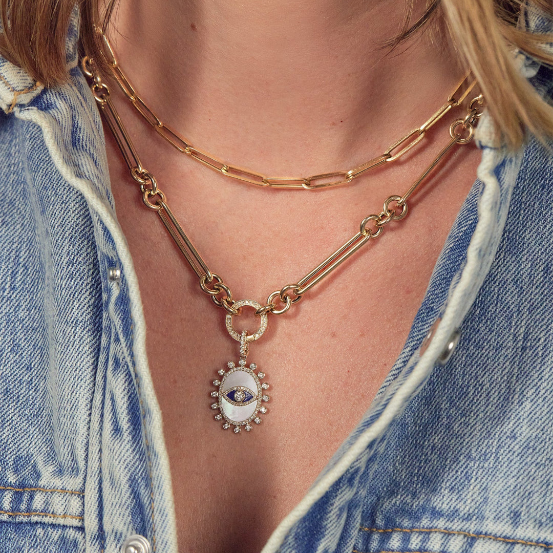 A person in a denim shirt wearing a 14k gold necklace with a double-sided diamond enhancer, featuring oval and round link chains with a mother of pearl pendant attached and a shorter gold paperclip chain necklace.
