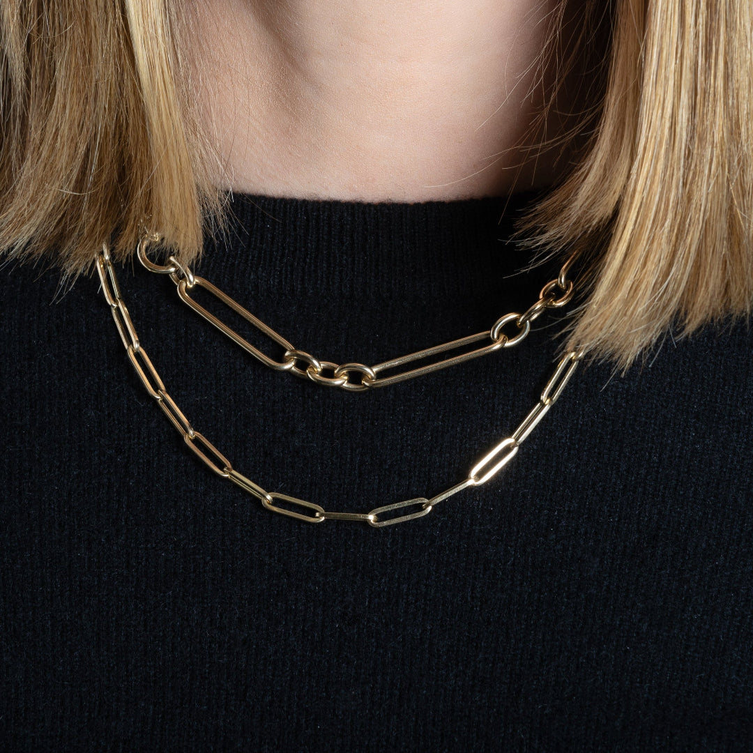 A person wearing a gold paperclip chain layered with a chunky mixed link chain.