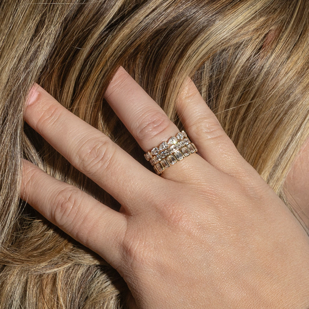 A person pulling their hair back from their face showcasing three stacking diamond band rings of different shaped diamonds set in 14k gold.