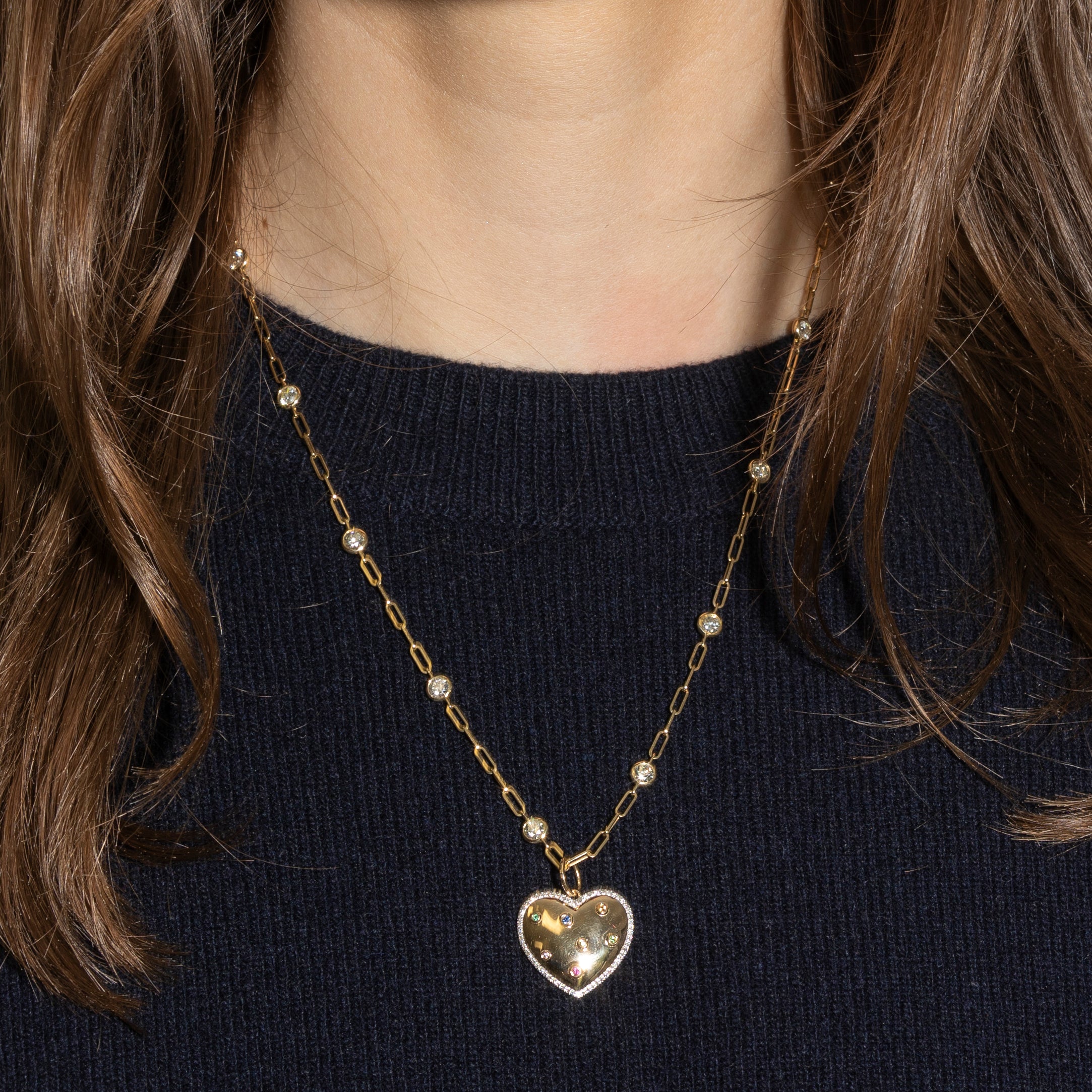 Gold heart-shaped pendant necklace on a person wearing a dark blue sweater.