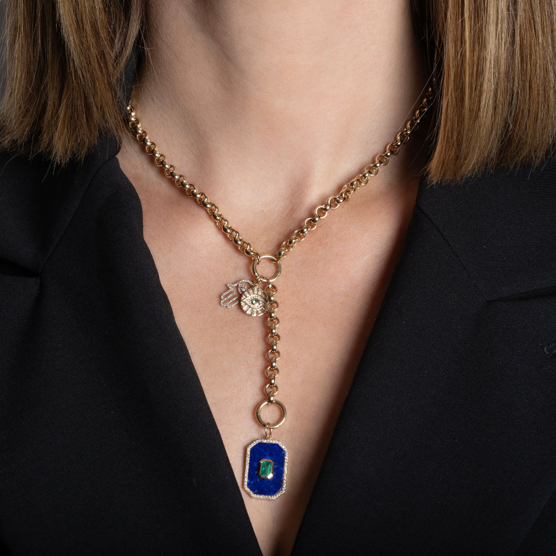 A person wearing 14k gold rolo lariat necklace with a 14k gold Hamsa diamond mini pendant and a larger lapis, emerald and diamond rectangle pendant.
