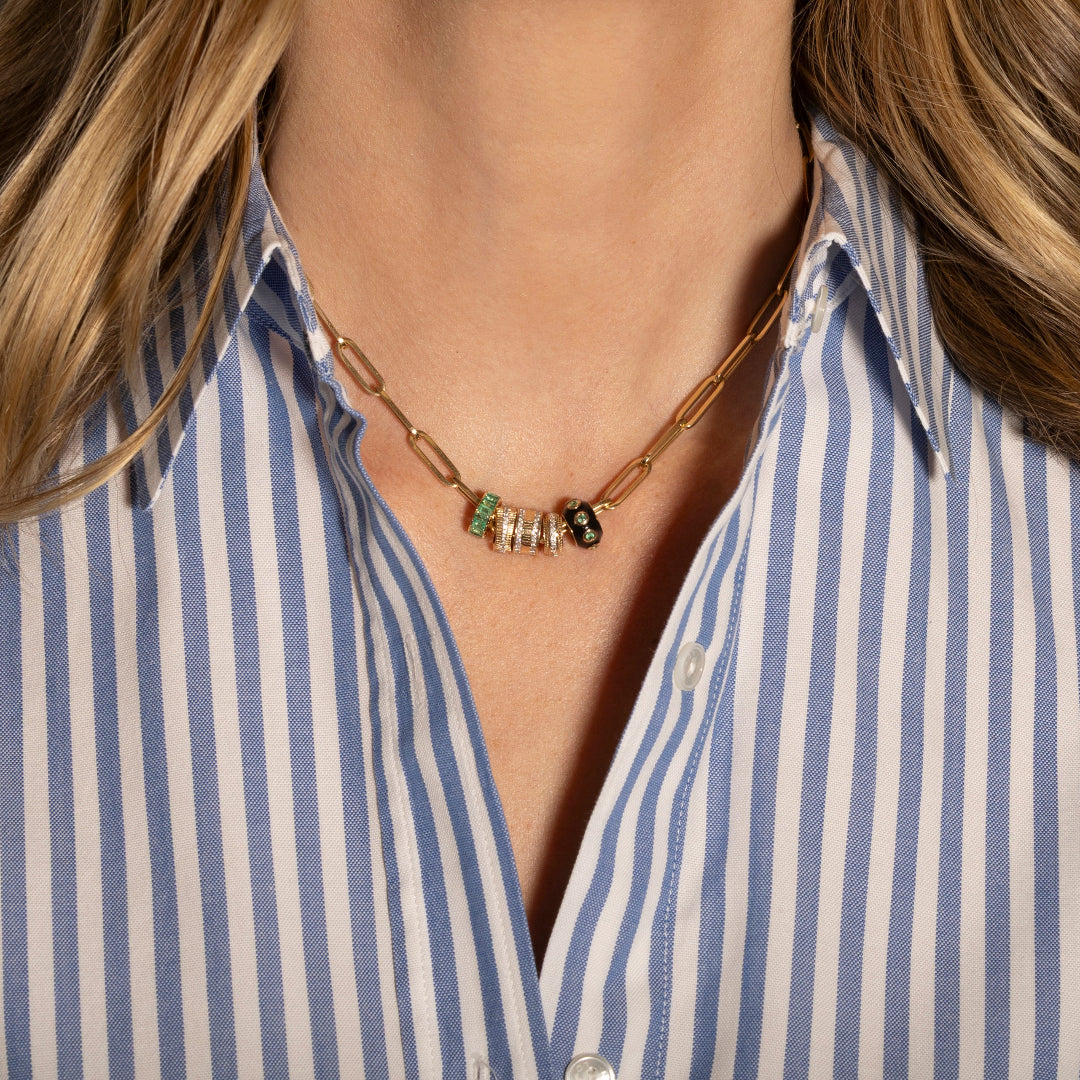 Necklace with green and black beads worn by a person in a blue and white striped shirt.
