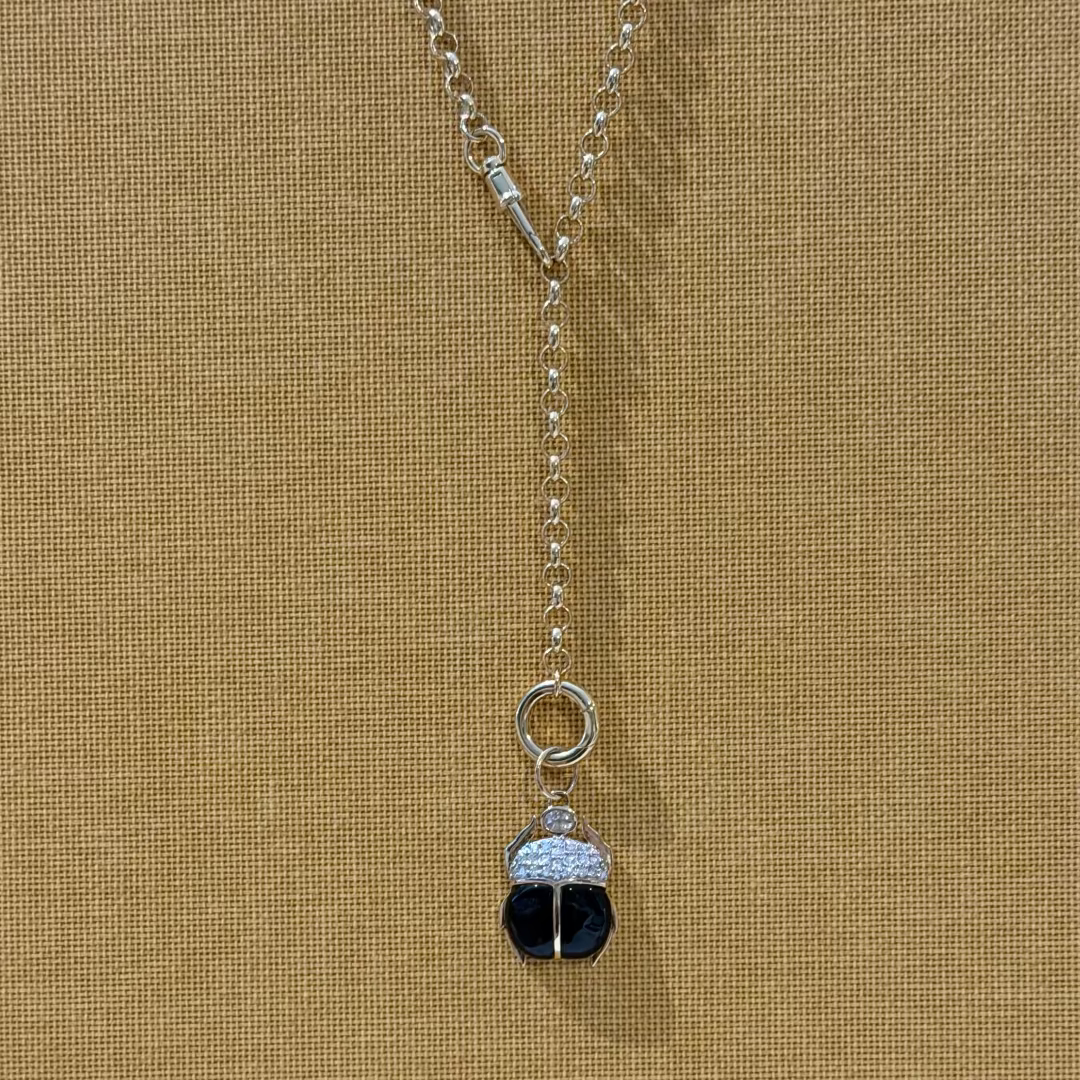 A 14k gold rolo chain with a onyx and diamond scarab pendant on a yellow textured background.
