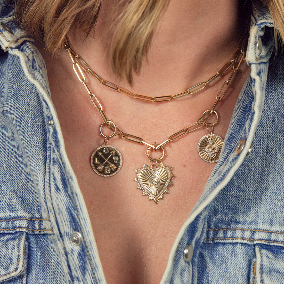 A person wearing two layered 14k paperclip chain necklaces, one adorned with charms.