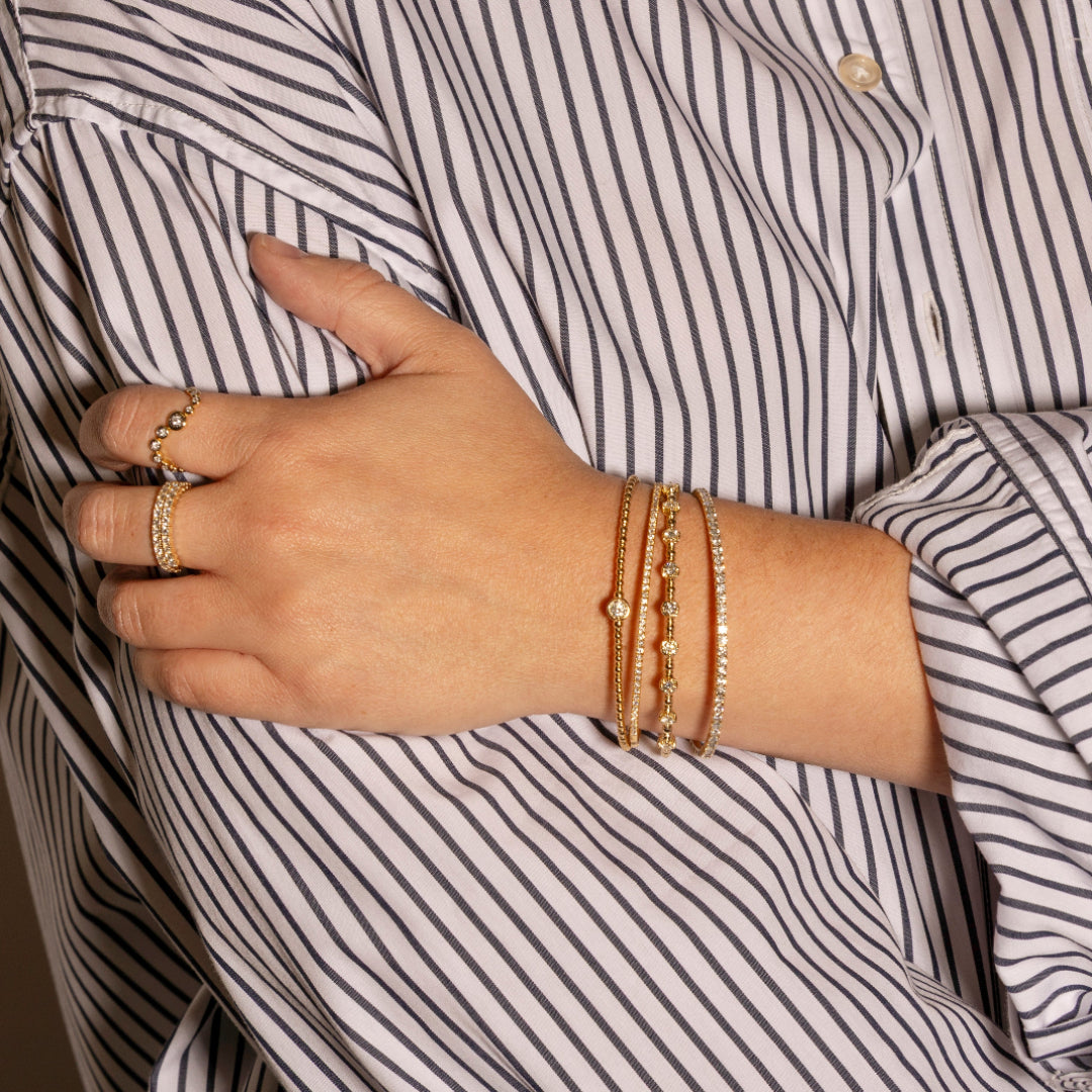 Hand wearing gold bracelets and rings with a striped shirt background
