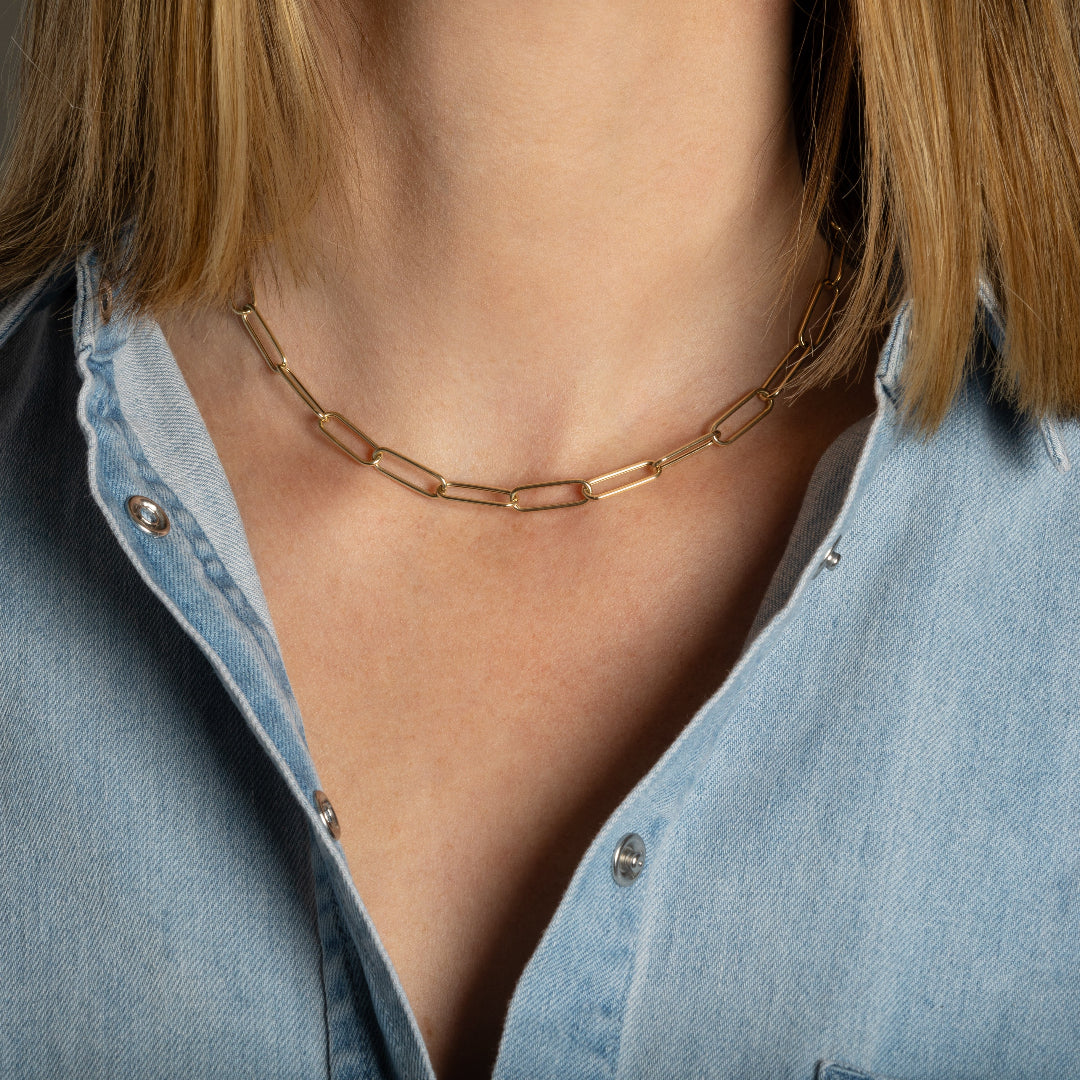 A person wearing a blue denim shirt modeling a 14k gold slim paperclip chain.