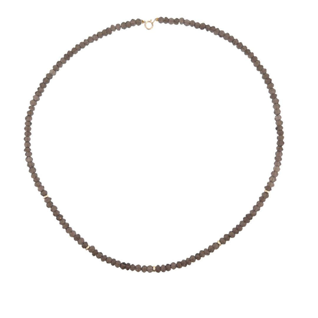 A beaded necklace made of small, faceted snoky quartz beads, arranged in an oval shape on a plain white background.