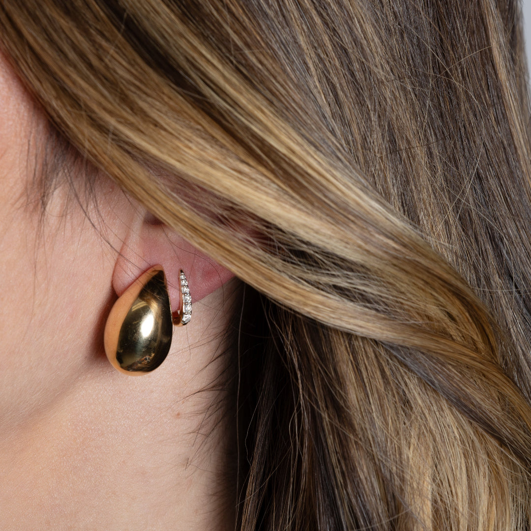 A person wearing two earrings, one tierdrop and one claw huggie earring.