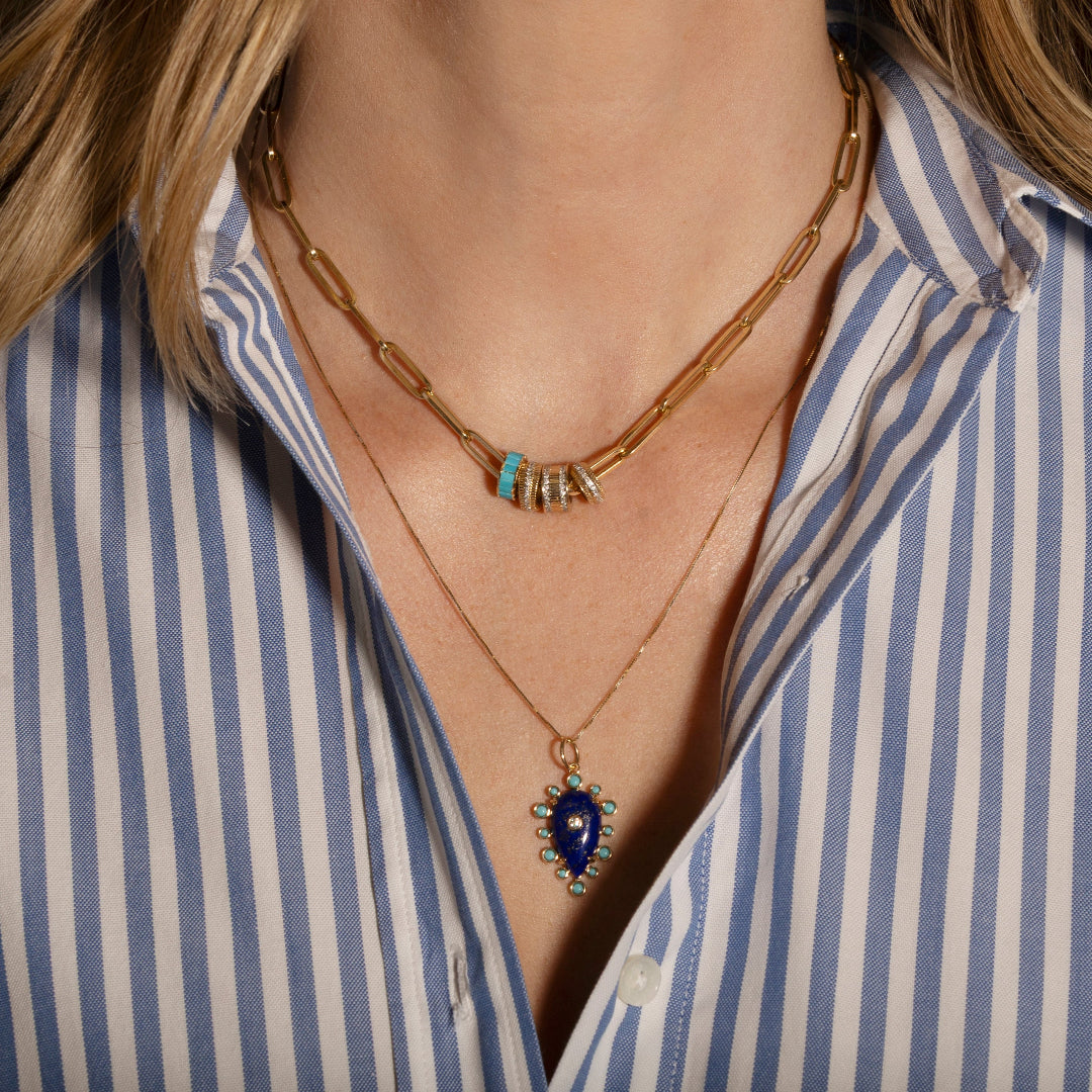 Necklace with a blue gemstone pendant worn by a person in a striped shirt