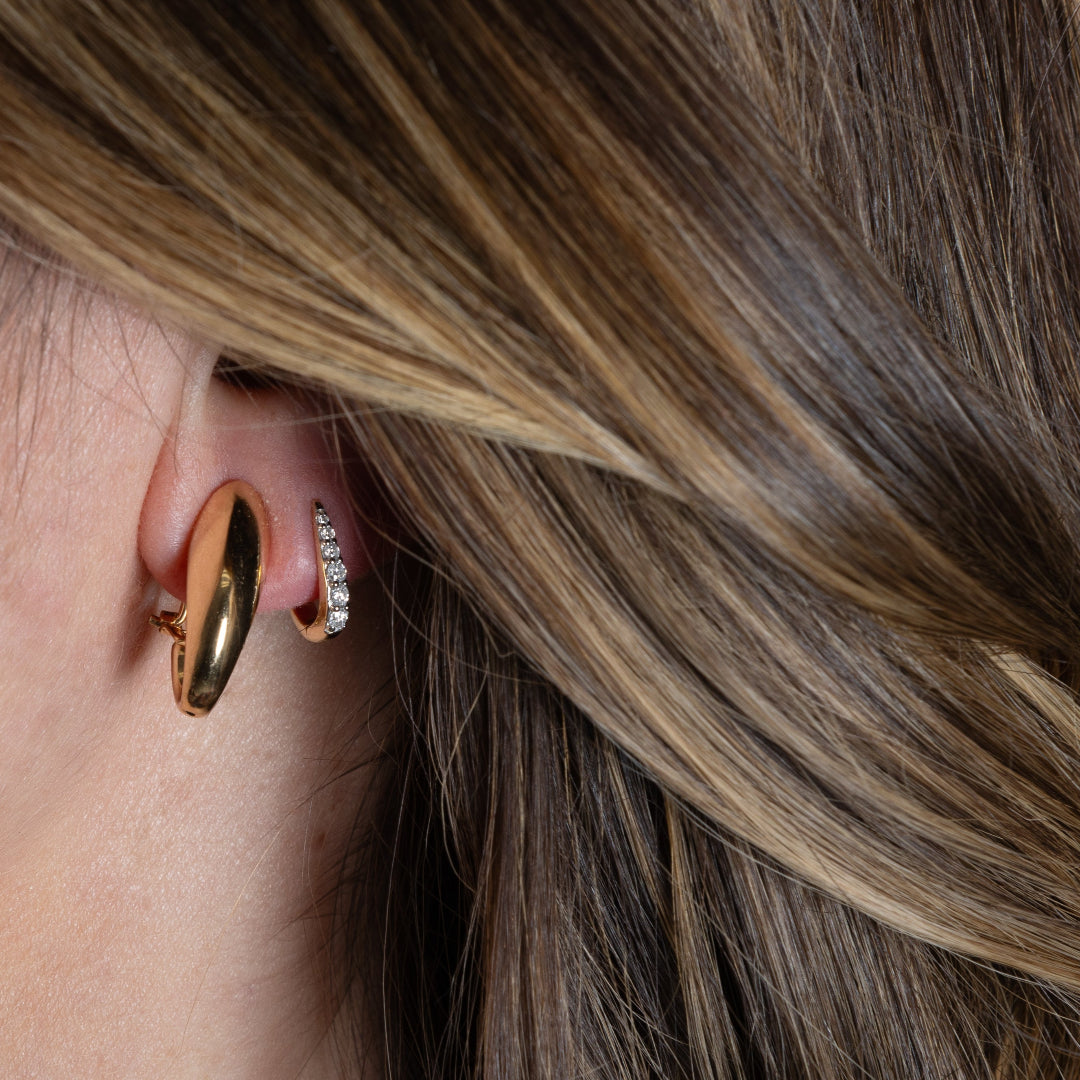 A person wearing two earrings, one is a removable part of the three link earrings and one is a claw huggie earring.